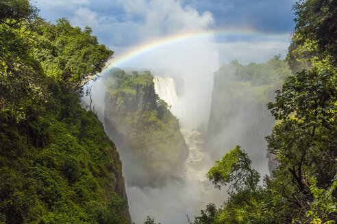 Blick von oben auf einen Wasserfall, der über bewachsene Felsen herabstürzt, einzelner Regenbogen. - MINF06619