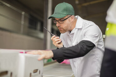 Arbeiter in einer Fabrik, die eine Box überprüfen und ein Walkie Talkie benutzen - ZEF15956