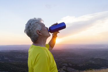 Spain, Catalonia, Montcau, senior man drinking water and looking at view from top of hill during sunset - AFVF01355