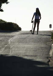 Junge Frau steht auf einer Straße und hält ein Skateboard. - MINF06627