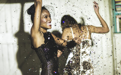 Two women wearing cocktail dresses at a party dancing in a shower of glitter confetti. - MINF06666