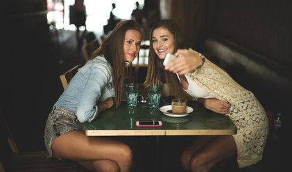 Zwei junge Frauen, die an einem Cafétisch sitzen und für ein Selfie posieren. - MINF06688