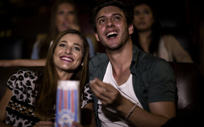 Zwei junge Leute sitzen in einem Kino, sehen einen Film und essen Popcorn. - MINF06693