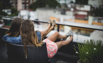 Two young women sitting on a rooftop with their arms around each other. - MINF06694