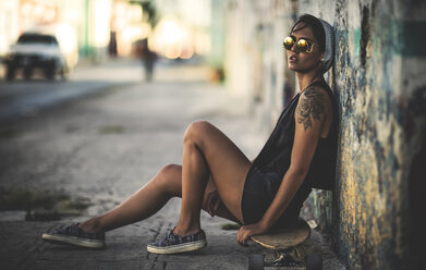 Junge Frau sitzt auf einem Skateboard auf der Straße. - MINF06699
