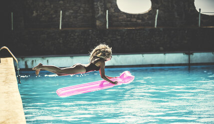 A young woman wearing a swimsuit jumping into a swimming pool holding a pool raft. - MINF06727