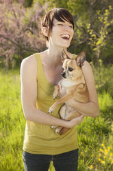 Young woman in grassy field in spring holding dog - MINF06741