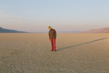 Die Landschaft der Black Rock Desert in Nevada. Ein Mann mit einer Tiermaske, die einen langen Schatten auf den Boden wirft. - MINF06746