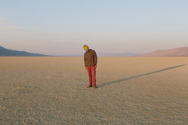 The landscape of the Black Rock Desert in Nevada. A man wearing an animal mask. Casting a long shadow on the ground. - MINF06746