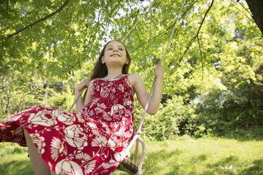 Sommer: Ein Mädchen im Sommerkleid auf einer Schaukel, die an den Ästen eines Baumes hängt. - MINF06761