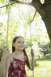 Sommer: Ein Mädchen im Sonnenkleid auf einer Schaukel in einem Obstgarten. - MINF06762