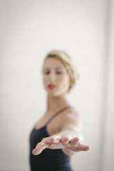 Eine blonde Frau in einem schwarzen Trikot steht in einem Raum und macht Yoga, den Arm ausgestreckt. - MINF06795