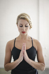 Eine blonde Frau in einem schwarzen Trikot macht Yoga, steht mit geschlossenen Augen und zusammengelegten Händen. - MINF06798