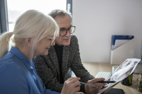 Two senior colleagues working together at desk in office examining photos - AWF00175