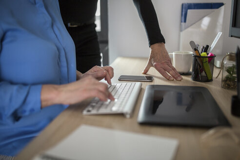 Close-up of two colleagues working together at desk in office - AWF00184