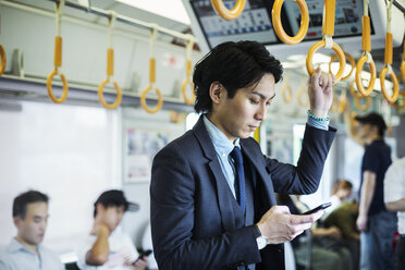 Businessman wearing suit standing on a commuter train, holding mobile phone. - MINF06807