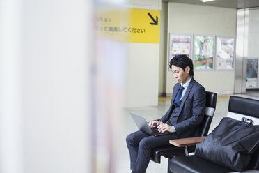 Businessman wearing suit sitting at train station, working on laptop. - MINF06808