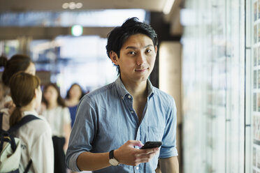 Businessman wearing blue shirt, holding mobile phone, looking at camera. - MINF06821