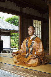 Buddhistischer Mönch mit kahlgeschorenem Kopf in goldener Robe, im Schneidersitz auf dem Boden sitzend, meditierend, buddhistische Handgeste. - MINF06842