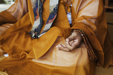 Nahaufnahme eines buddhistischen Mönchs in goldener Robe, der im Schneidersitz auf dem Boden sitzt und meditiert, buddhistische Handgesten. - MINF06843