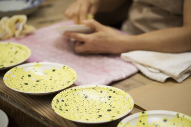 Close up of person working in a Japanese porcelain workshop, applying yellow glaze to white plates. - MINF06846