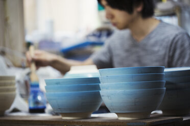 Close up of man working in a Japanese porcelain workshop, painting white bowls with blue glaze. - MINF06847