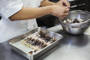 Nahaufnahme eines Kochs bei der Arbeit in der Küche eines japanischen Sushi-Restaurants, der Torigai, große Herzmuscheln, in ein Metalltablett legt. - MINF06854