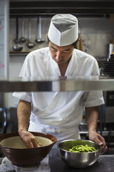 Koch in der Küche eines japanischen Sushi-Restaurants, der eine Schüssel mit Edamame-Bohnen zubereitet. - MINF06855