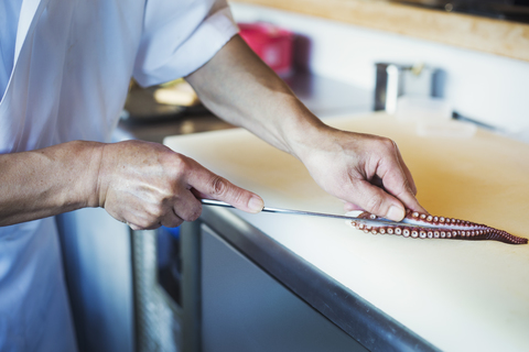 Nahaufnahme eines Kochs, der in einem japanischen Sushi-Restaurant an einem Tresen arbeitet und einen Tintenfischtentakel aufschneidet., lizenzfreies Stockfoto