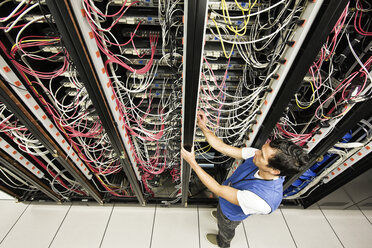 Caucasian male technician working on a CAT 5 cable bundling system in a large computer server room. - MINF06883