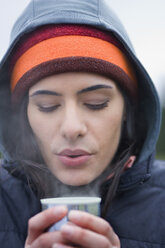 Kaukasische Frau, die an einem Wintertag auf die Oberfläche einer heißen Tasse Kaffee bläst. - MINF06924