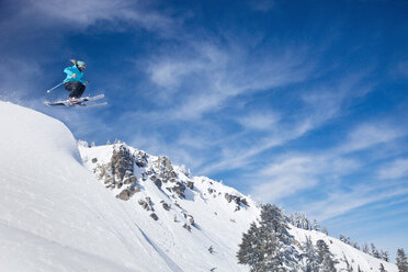 Eine Skifahrerin, die sich in den frischen Pulverschnee stürzt, mit Bergen und blauem Himmel im Hintergrund. - AURF00009