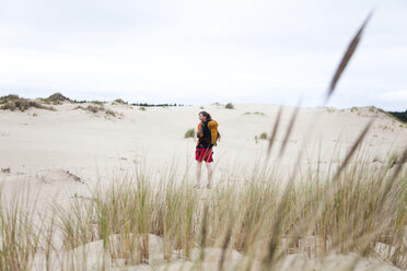 A girl walks alone on the sand dunes wearing a backpack. - AURF00029