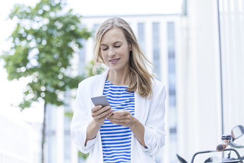 Lächelnde blonde Geschäftsfrau mit Smartphone, lizenzfreies Stockfoto