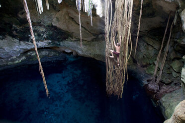 Young man climbing long, hanging vines above the cenotes of Mexico's Yucatan Peninsula. - AURF00037