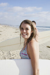 Eine junge Surferin steigt mit ihrem Surfbrett in der Hand aus dem Wasser, schaut in die Kamera und lächelt am Pacific Beach, San Diego, Kalifornien. - AURF00051