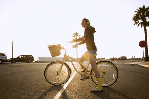 Eine junge Frau mit Kopfhörern, gelben Socken und Kapuzenpulli fährt mit einem Cruiser-Fahrrad zum Strand. - AURF00058