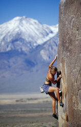 Junge Frau beim Bouldern in der Sonne mit schneebedecktem Berghintergrund. - AURF00061