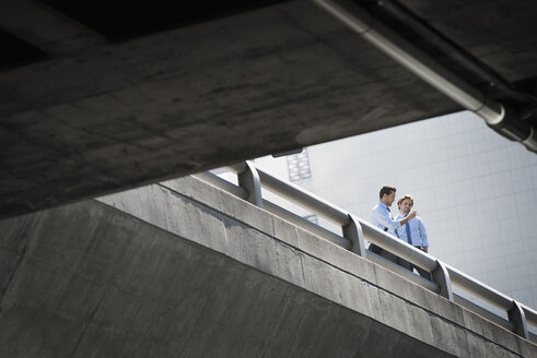 Zwei Geschäftsleute stehen an ein Geländer gelehnt auf einem städtischen Gehweg, Blick von unten. - MINF06977