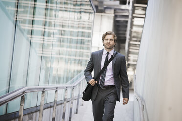 A man carrying a computer bag with a strap on a city walkway. - MINF06984