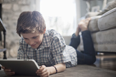 A boy lying on his front on the floor, looking at a digital tablet. - MINF06993