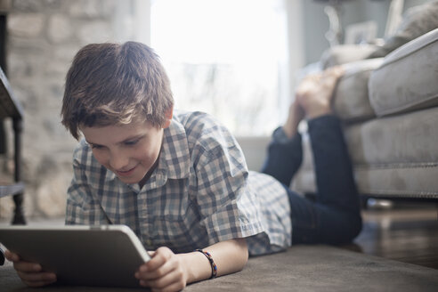 Ein Junge liegt auf dem Rücken auf dem Boden und schaut auf ein digitales Tablet. - MINF06993