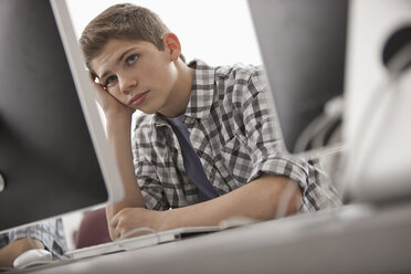 Ein Schulraum, ein Computerlabor oder ein Labor mit Reihen von Computermonitoren und Sitzgelegenheiten. Ein Junge sitzt mit der Hand am Kinn und sieht genervt aus. - MINF07007
