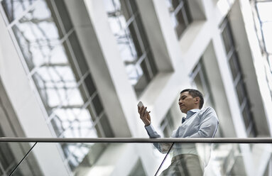 A man checking his smart phone in a large airy building with windows. - MINF07018