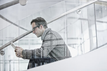 A man seated on steps using a digital tablet. - MINF07026