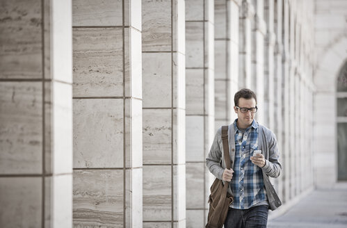 Ein Mann vor einem Gebäude, der sein Smartphone überprüft. - MINF07028