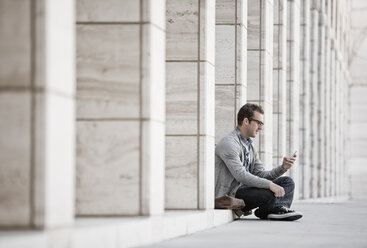 A man outside a building, checking his smart phone. - MINF07029