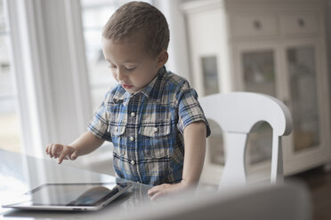 A young child sitting at a table using a digital tablet with a touchscreen. - MINF07036