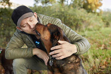 Dog walker bending down to stroke a dog nuzzling his face. - MINF07099