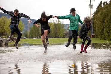 Young adults jump and splash in a large puddle - AURF00100